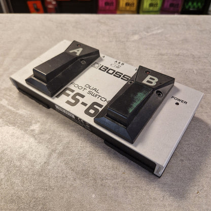 Pre-Owned Boss Dual Foot Switch FS-6 Pedal A BOSS FS-6 dual foot switch pedal with black switches on a silver metal base, photographed on a gray textured surface.