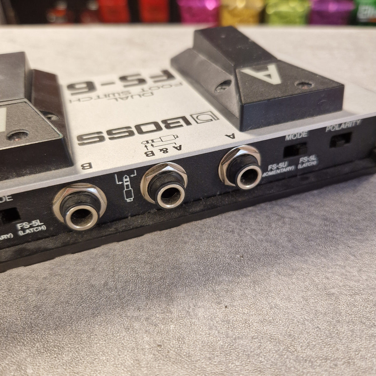 Pre-Owned Boss Dual Foot Switch FS-6 Pedal Close-up of a Boss FS-6 dual foot switch pedal, showing the front jacks, switches, and foot pedals on a gray textured surface.