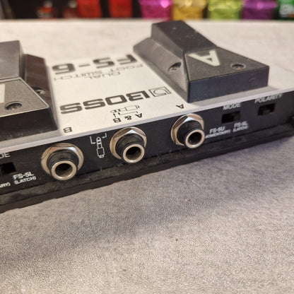 Pre-Owned Boss Dual Foot Switch FS-6 Pedal Close-up of a Boss FS-6 dual foot switch pedal, showing the front jacks, switches, and foot pedals on a gray textured surface.