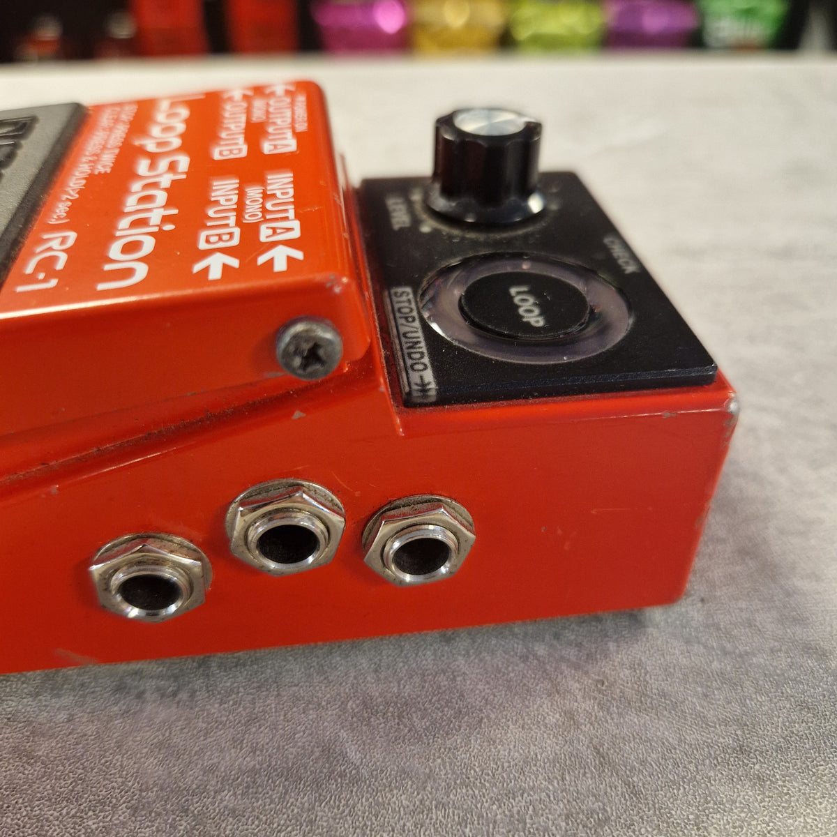 Pre-Owned Boss RC-1 Looper Pedal w/ Box - Close-up of a red Loop Station RC-1 guitar effects pedal with a black loop section, silver jacks, and white printed controls against a gray textured background.