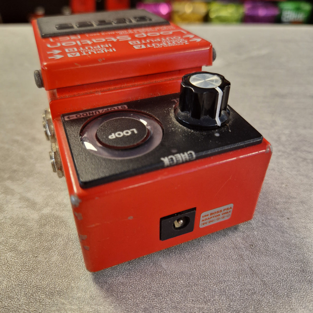Pre-Owned Boss RC-1 Looper Pedal w/ Box - A red and black guitar effects pedal, likely a Wah-Wah or echo effect unit, photographed on a textured gray surface with a blurred background.