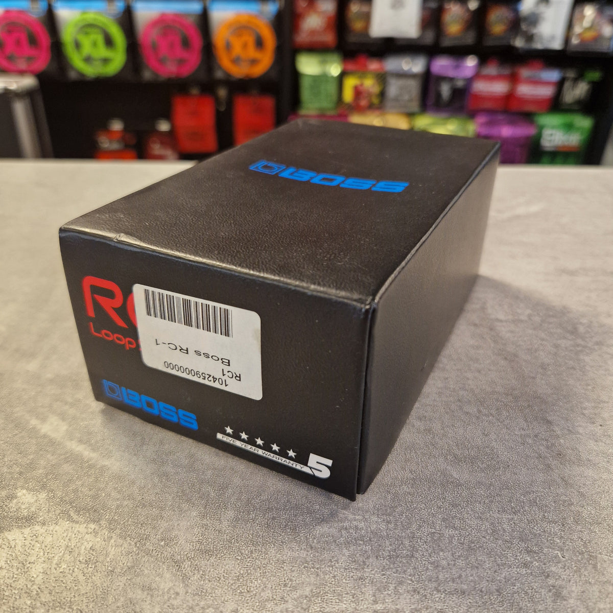 Pre-Owned Boss RC-1 Looper Pedal w/ Box A black rectangular product box with blue and red Diags branding, photographed on a gray textured surface with a blurred store shelf in the background.