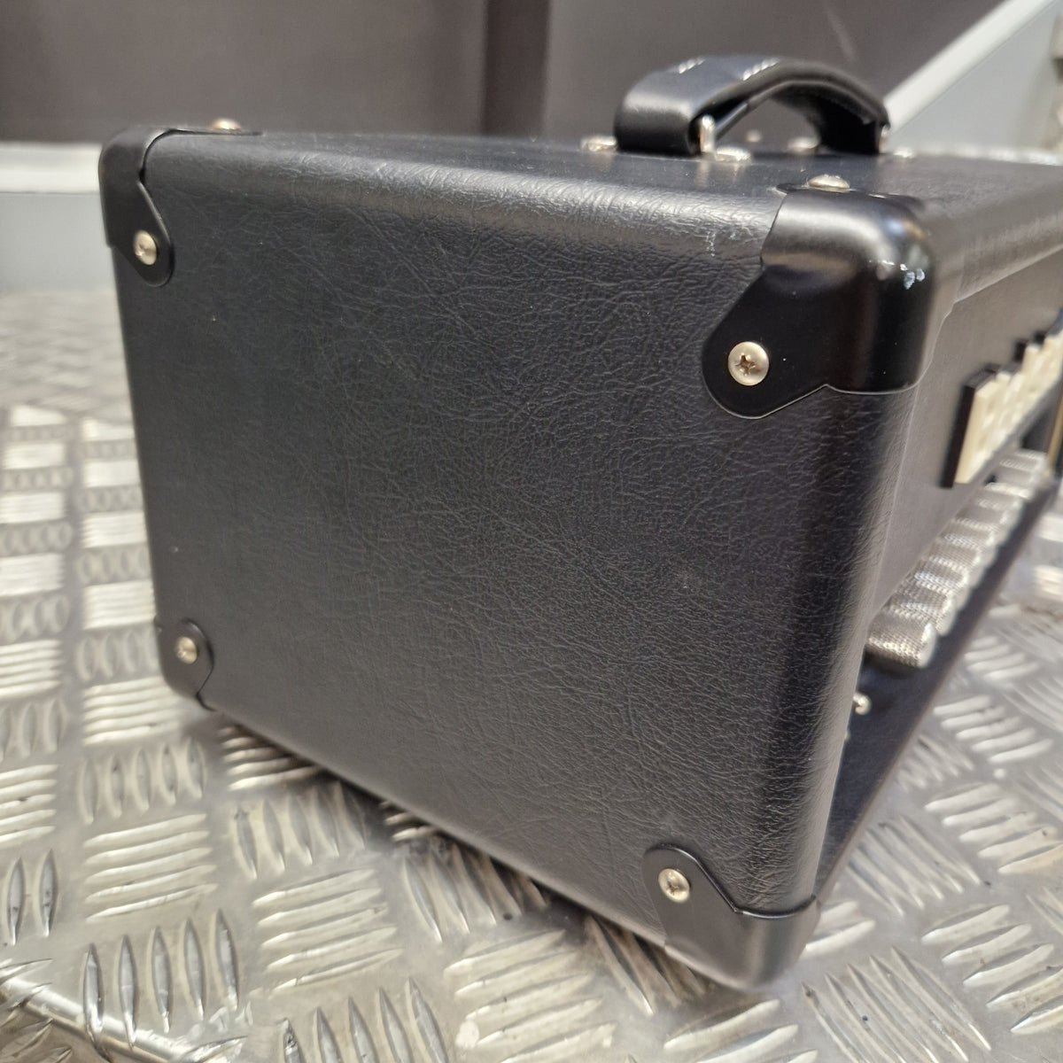 Pre-Owned Blackstar HT-5RH 5w Electric Amplifier Head w/ Footswitch - Close-up of the bottom corner of a black textured guitar amplifier, showing the corner protectors and handle attachment, resting on a silver diamond plate metal surface.