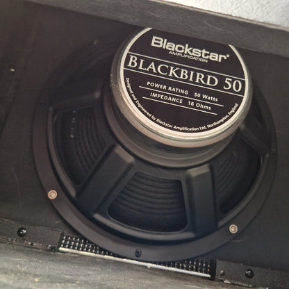 Pre-Owned Blackstar HT-112 1x12 Electric Amplifier Cab - A close-up of a Blackstar Blackbird 50 speaker driver inside a black amplifier cabinet, showing the brand label and part of the cone.
