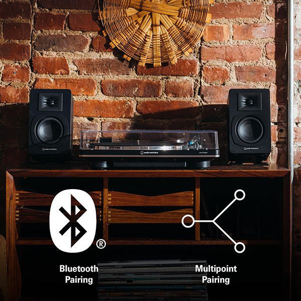 Audio-Technica AT-SP3X Audio equipment on a wooden shelf with Bluetooth and multipoint pairing icons.