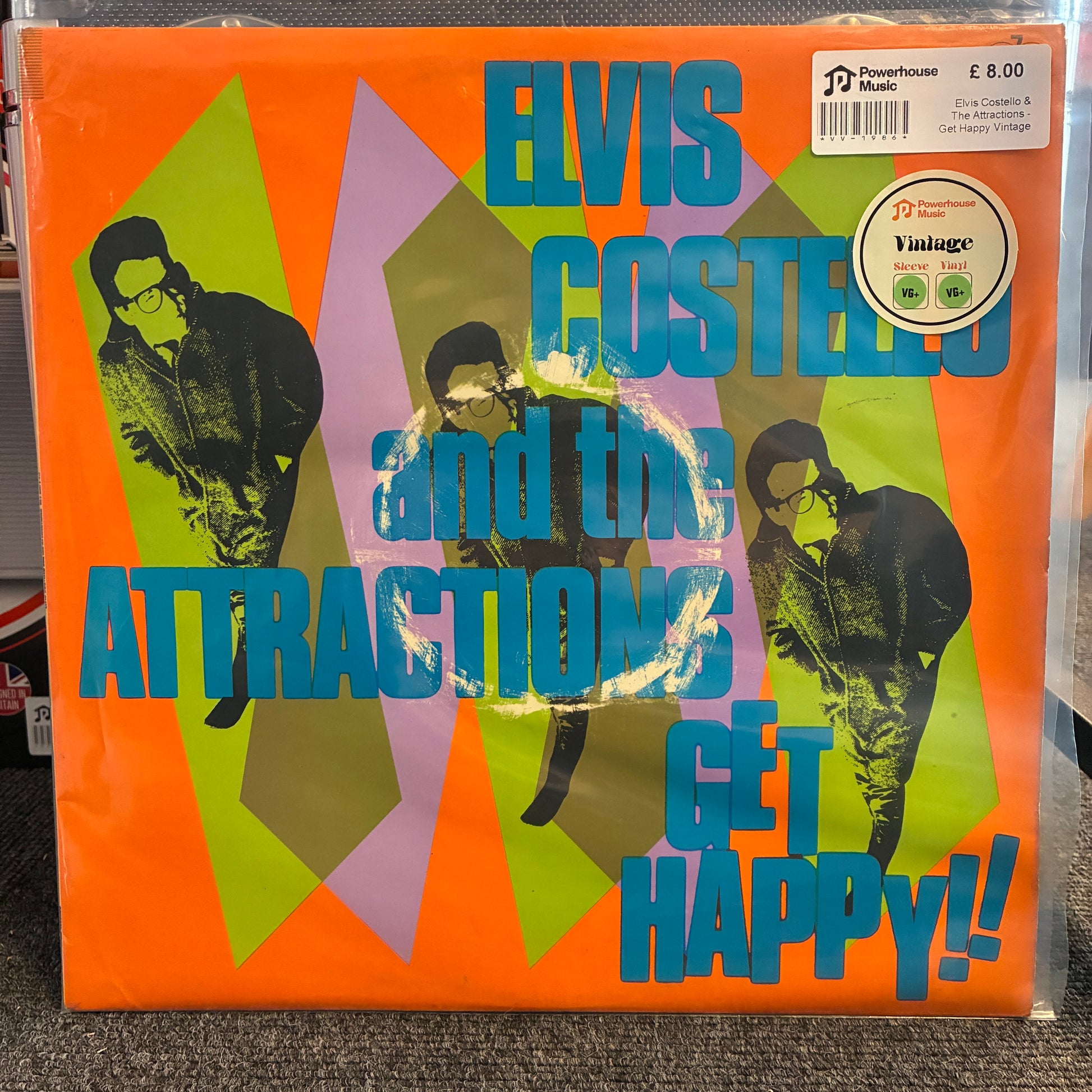 Elvis Costello And The Attractions - Get Happy Vintage Vinyl LP Elvis Costello and the Attractions - Get Happy!! vinyl record album cover, showing three black-and-white photos of Elvis with blue text over an orange, green, and purple geometric background. A 'Pioneer' 12-inch single cover sticker is visible in the top right.