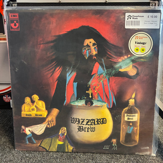 Wizzard - Wizzard Brew Vintage Vinyl LP Jazz Brew vinyl record album cover in a clear plastic protective sleeve, photographed standing on a gray carpet. The cover art shows a dark-haired figure in front of a cauldron with the title 'Jazz Brew' and smaller illustrated scenes around it.