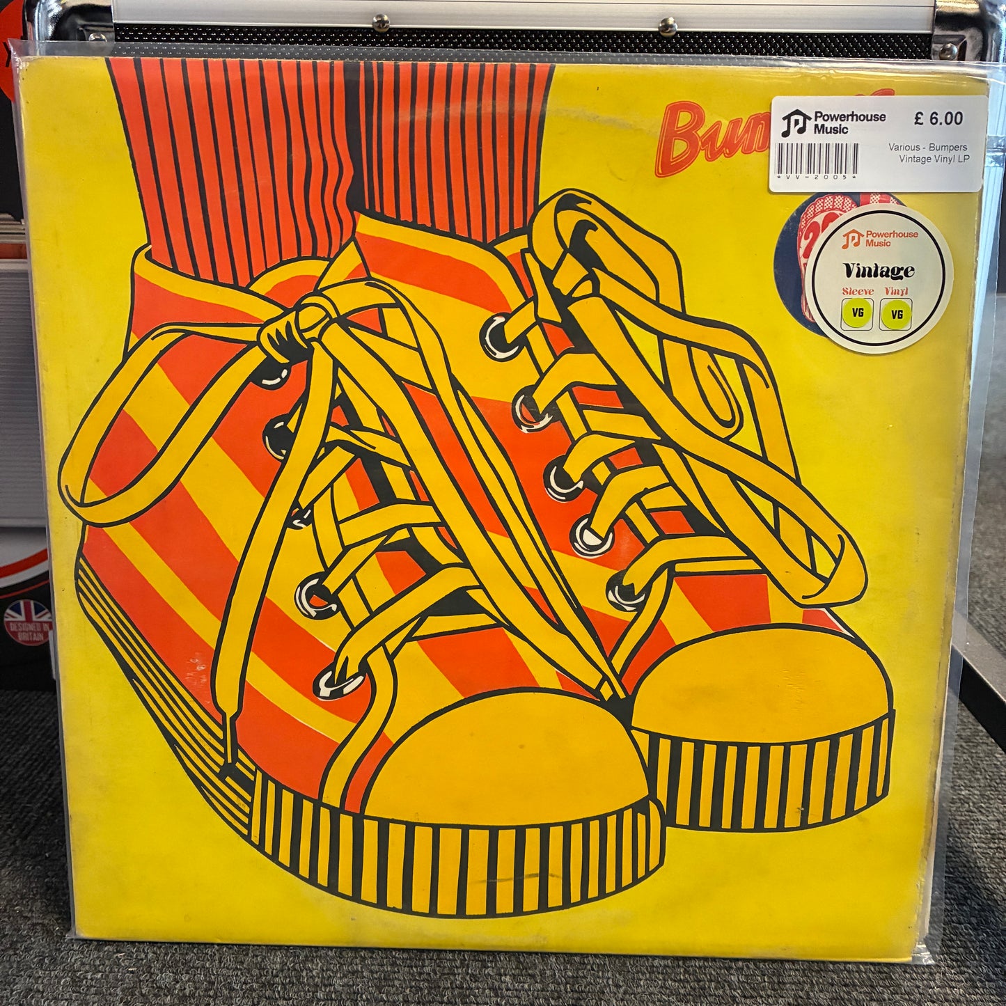 Various - Bumpers Vintage Vinyl LP A vinyl record sleeve for Budgie's 'Bugs' album, featuring a bold graphic illustration of yellow and orange striped high-top sneakers on a bright yellow background. The record is sealed in a clear plastic case with a Powerhouse label sticker and a barcode price tag visible.