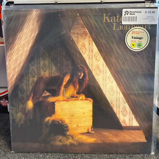 Kate Bush - Lionheart Vintage Vinyl LP Kate Bush's 'Lionheart' vinyl record album cover, showing a lion cub in a wooden crate inside a cave-like setting. The cover has a 'Vintage' 1990 reissue sticker and a 'Powerhouse' label sticker, photographed in a plastic sleeve.