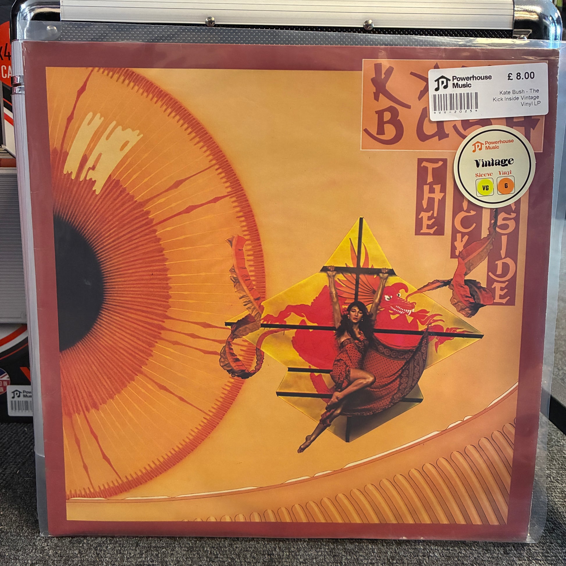 Kate Bush - The Kick Inside Vintage Vinyl LP Kurt Cobain's 'The Cyber Side' vinyl record album in a clear protective plastic sleeve, resting on a gray carpeted shelf. The album cover features a warm beige and orange background with a large stylized eye graphic and a central figure in a red and yellow vehicle.