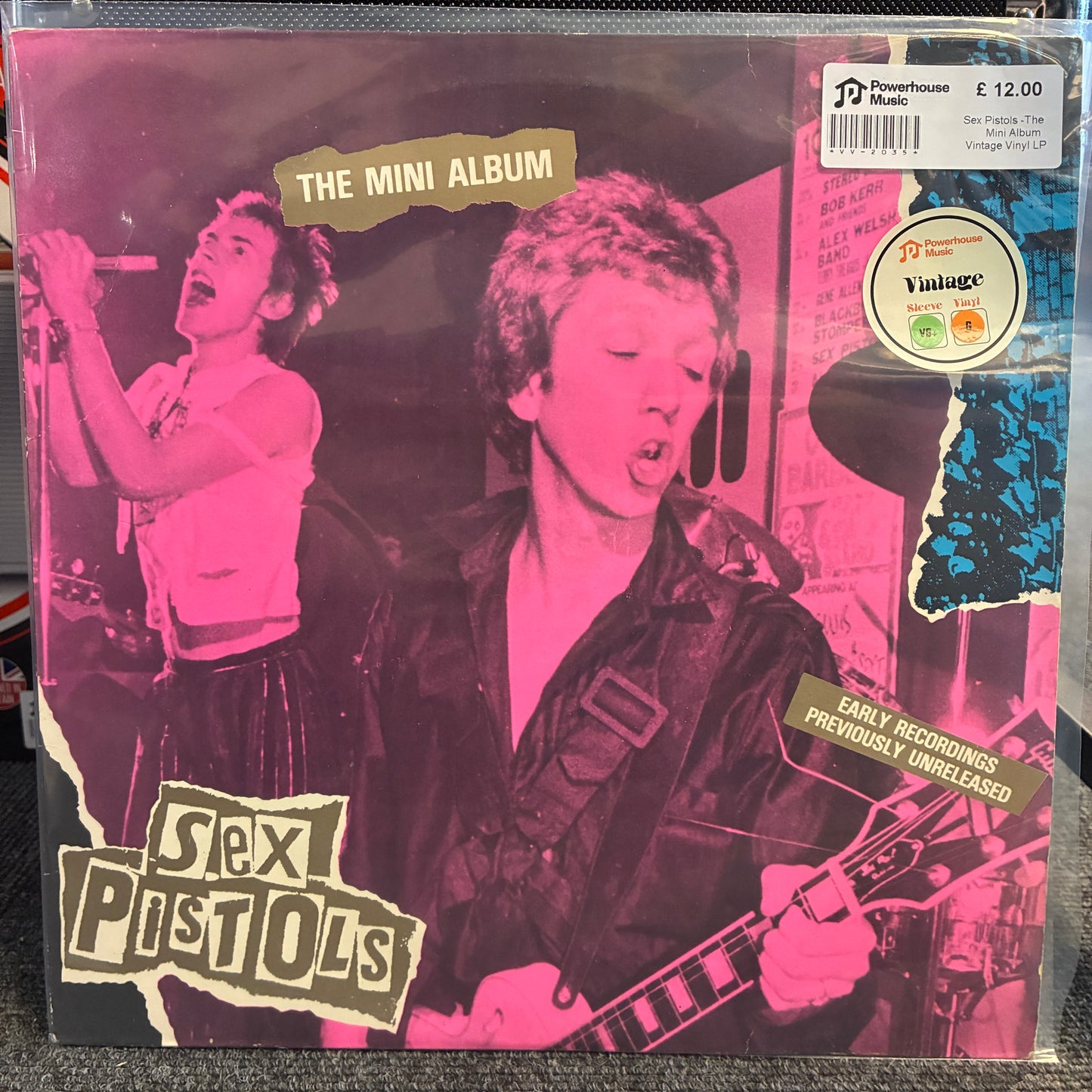 Sex Pistols -The Mini Album  Vintage Vinyl LP Sex Pistols 'The Mini Album' vinyl record cover, featuring a pink and black photo of the band members with torn-paper style text overlays. A white barcode sticker and a circular 'Vintage' label are visible on the top right.