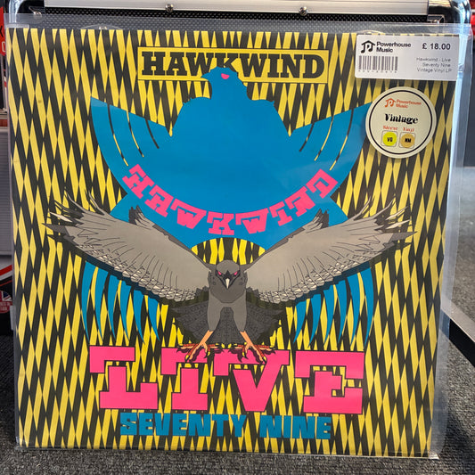 Hawkwind - Live Seventy Nine Vintage Vinyl LP A vinyl record sleeve for Hawkwind's 'Live Seventy Nine' is shown in a clear plastic sleeve, likely in a store setting. The cover art features a bold black and yellow zigzag pattern, a large blue bird silhouette, a smaller gray bird in the foreground, and pink text reading 'HAWKWind LIVE Seventy Nine'.