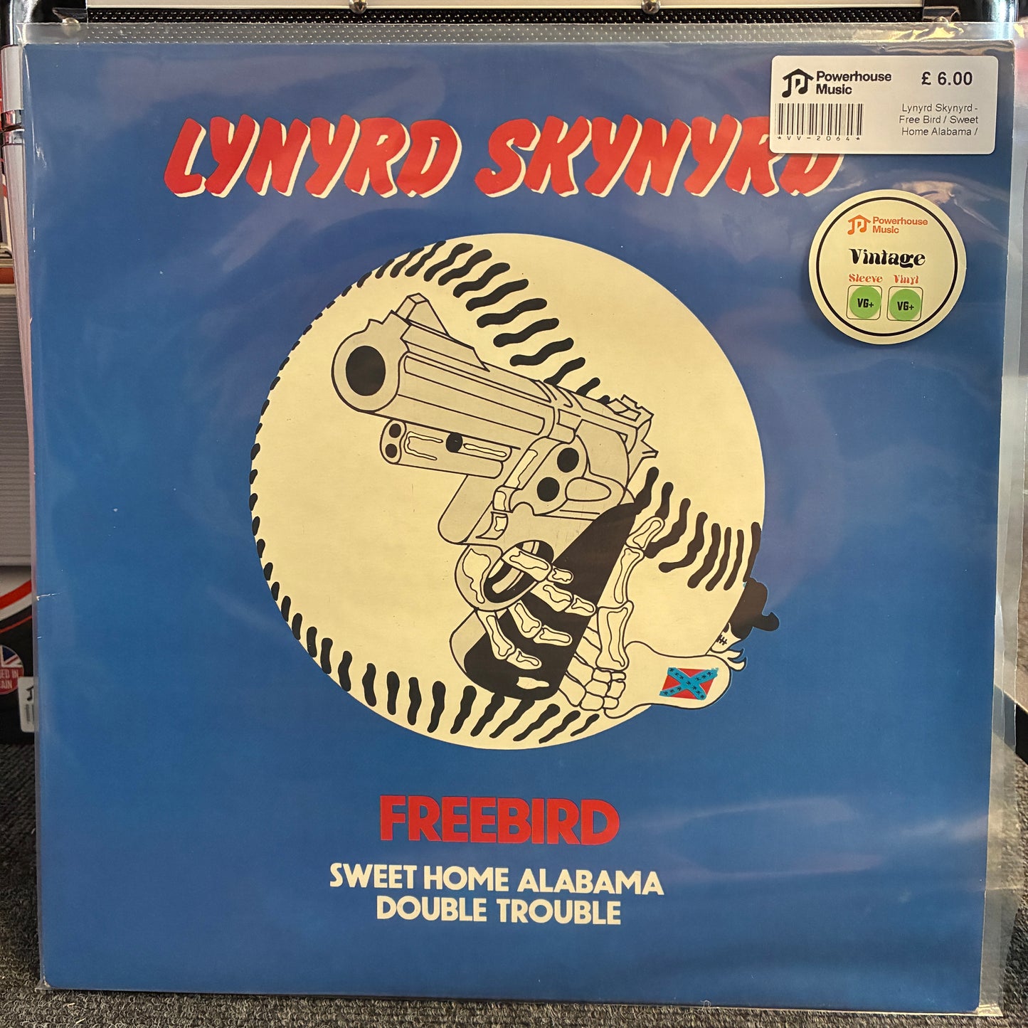 Lynyrd Skynyrd - Free Bird / Sweet Home Alabama / Double Trouble Vintage Vinyl 12" Single A vinyl record sleeve for Lynyrd Skynyrd's 'Freebird - Sweet Home Alabama Double Trouble' in blue, featuring a central circular graphic of a hand holding a revolver over a baseball-stripe pattern. A 'JD Powerhouse Music' sticker is visible in the top right corner.