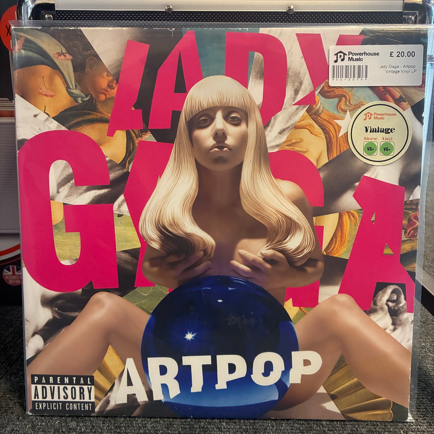 Lady Gaga - Artpop Vintage Vinyl LP A vinyl record sleeve for Lady Gaga's 'Art Pop' album, sealed in a clear plastic protective case. The cover art features a blonde woman with a blank face, large pink 'LADY GAGA' text, a blue reflective orb, and a 'Parental Advisory' label.