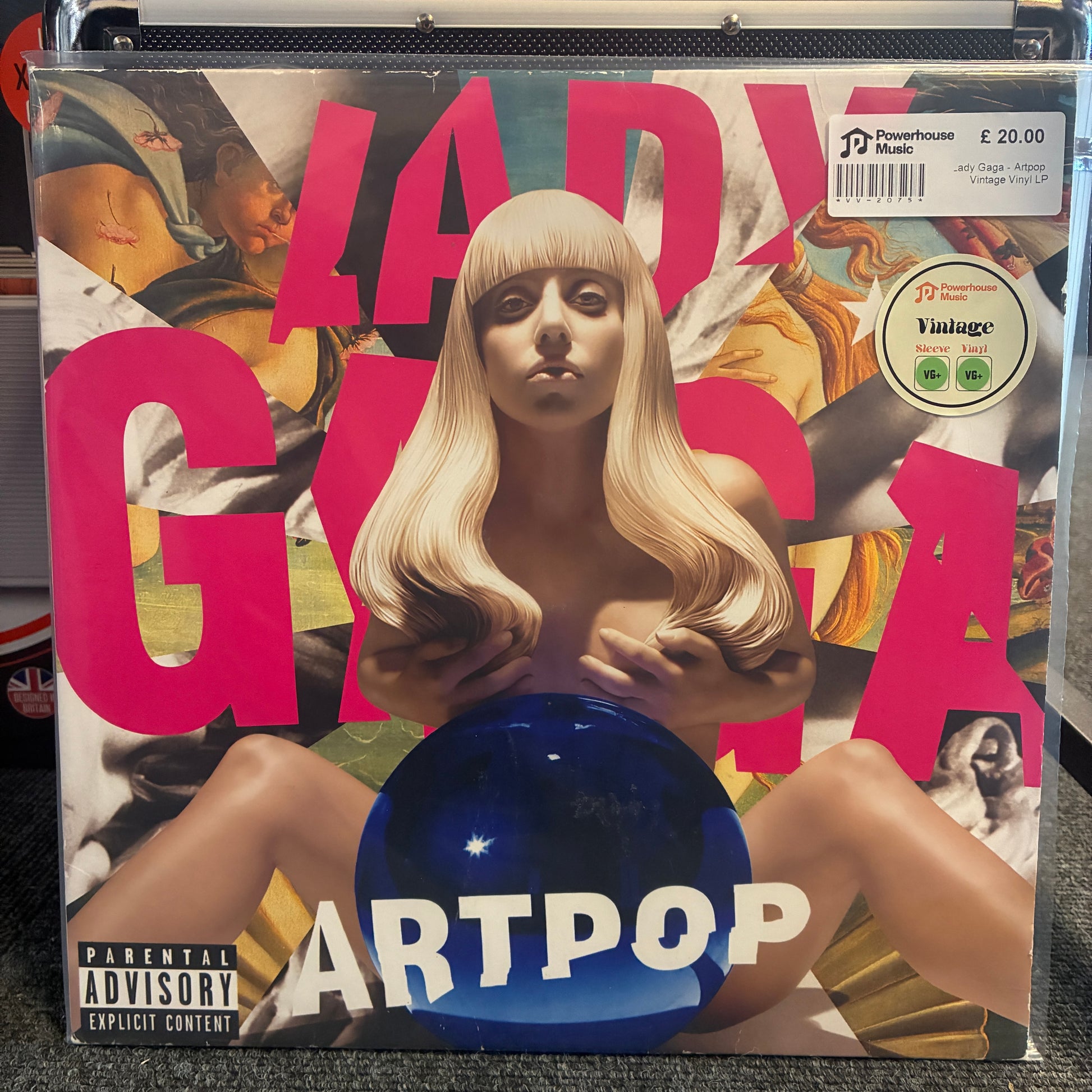 Lady Gaga - Artpop Vintage Vinyl LP A vinyl record sleeve for Lady Gaga's 'Art Pop' album, sealed in a clear plastic protective case. The cover art features a blonde woman with a blank face, large pink 'LADY GAGA' text, a blue reflective orb, and a 'Parental Advisory' label.