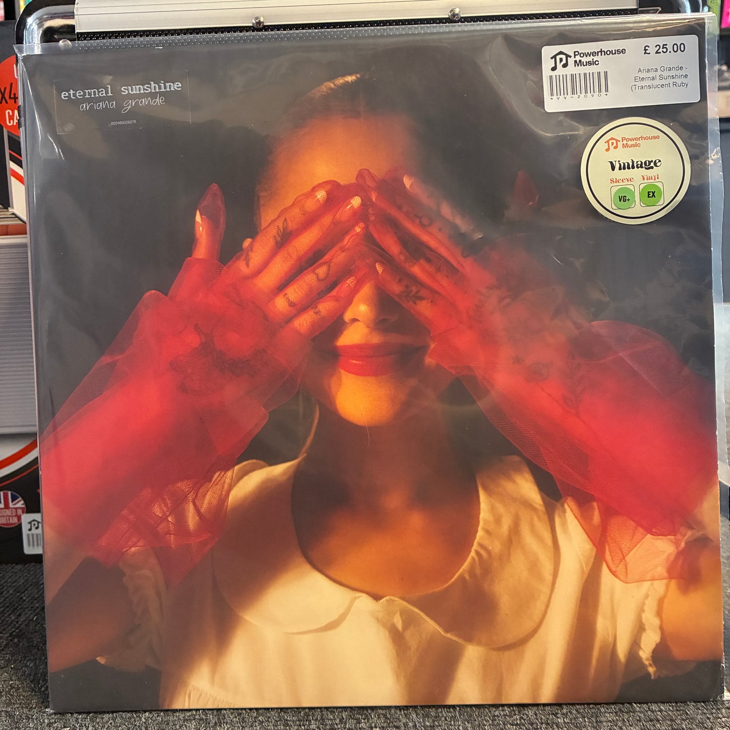 Ariana Grande - Eternal Sunshine (Translucent Ruby Red) Vintage Vinyl LP A vinyl record sleeve for the song 'eternal sunshine' by John Mayer, featuring a woman with red sheer gloves covering her eyes. The sleeve has a Powerhouse Music sticker and a Vintage vinyl sticker on the top right.