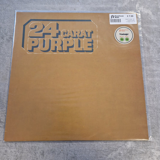 Deep Purple - 24 Carat Purple Vintage Vinyl LP A 24 Carat Purple vinyl record sleeve in its clear plastic shrink wrap, placed on a gray textured surface. The sleeve is a metallic gold color with the band's name printed in a stylized dark blue font.