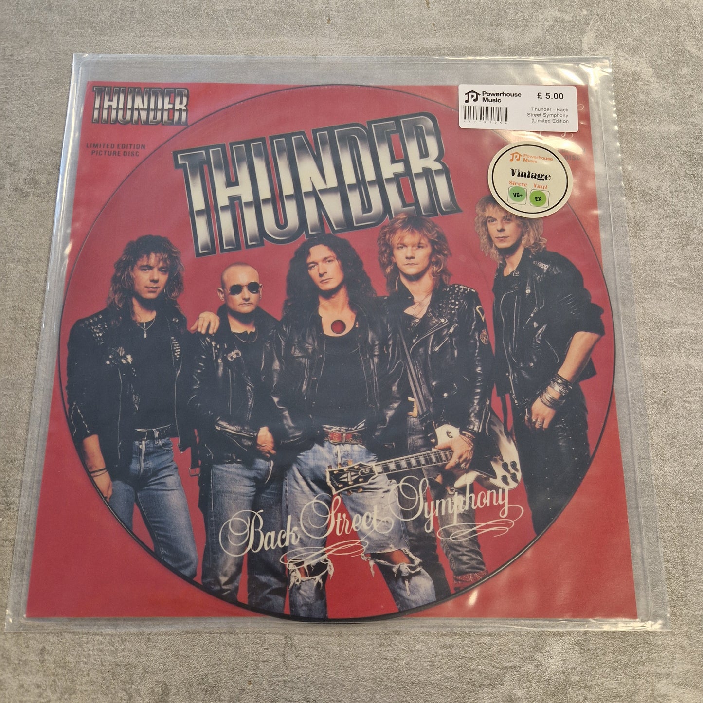 Thunder - Back Street Symphony (Limited Edition Picture Disc) Vintage Vinyl 12" Single A vinyl record sleeve for the band Thunder's 'Back To Hell' album, featuring a red circular design with the band members' photos and a Parental Advisory label, photographed in a clear plastic sleeve on a gray textured surface.