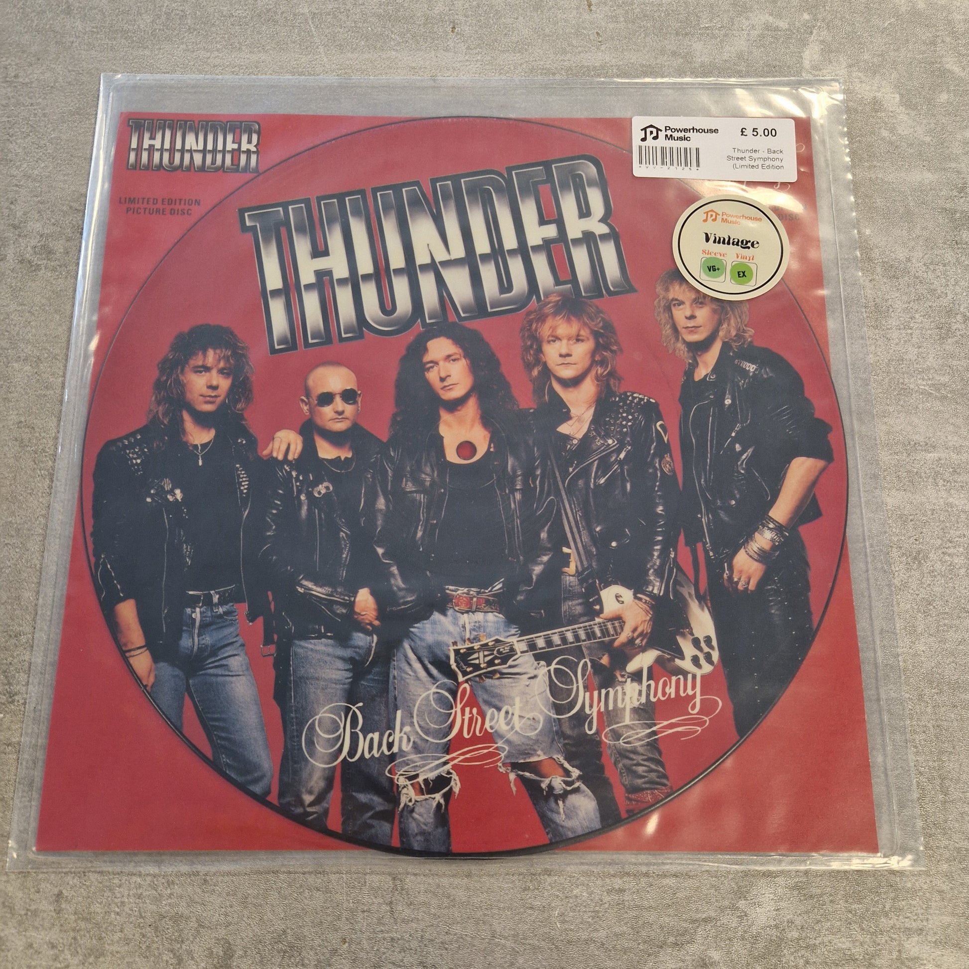 Thunder - Back Street Symphony (Limited Edition Picture Disc) Vintage Vinyl 12" Single A vinyl record sleeve for the band Thunder's 'Back To Hell' album, featuring a red circular design with the band members' photos and a Parental Advisory label, photographed in a clear plastic sleeve on a gray textured surface.
