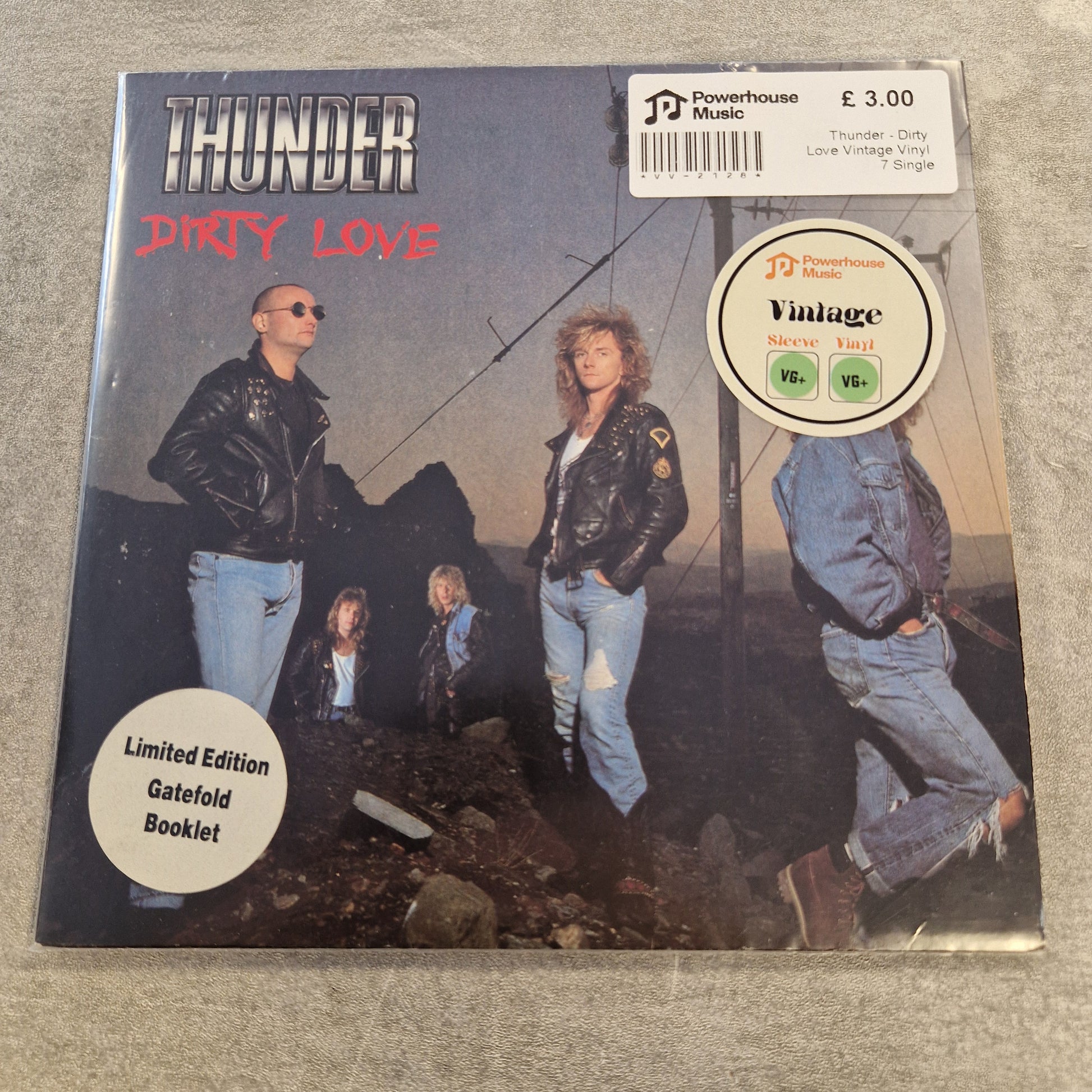 Thunder - Dirty Love Vintage Vinyl 7" Single A physical copy of the band Thunder's 'Dirty Love' 12-inch vinyl record album, featuring a cover with multiple photos of the band members and sticker overlays, placed on a gray textured surface.