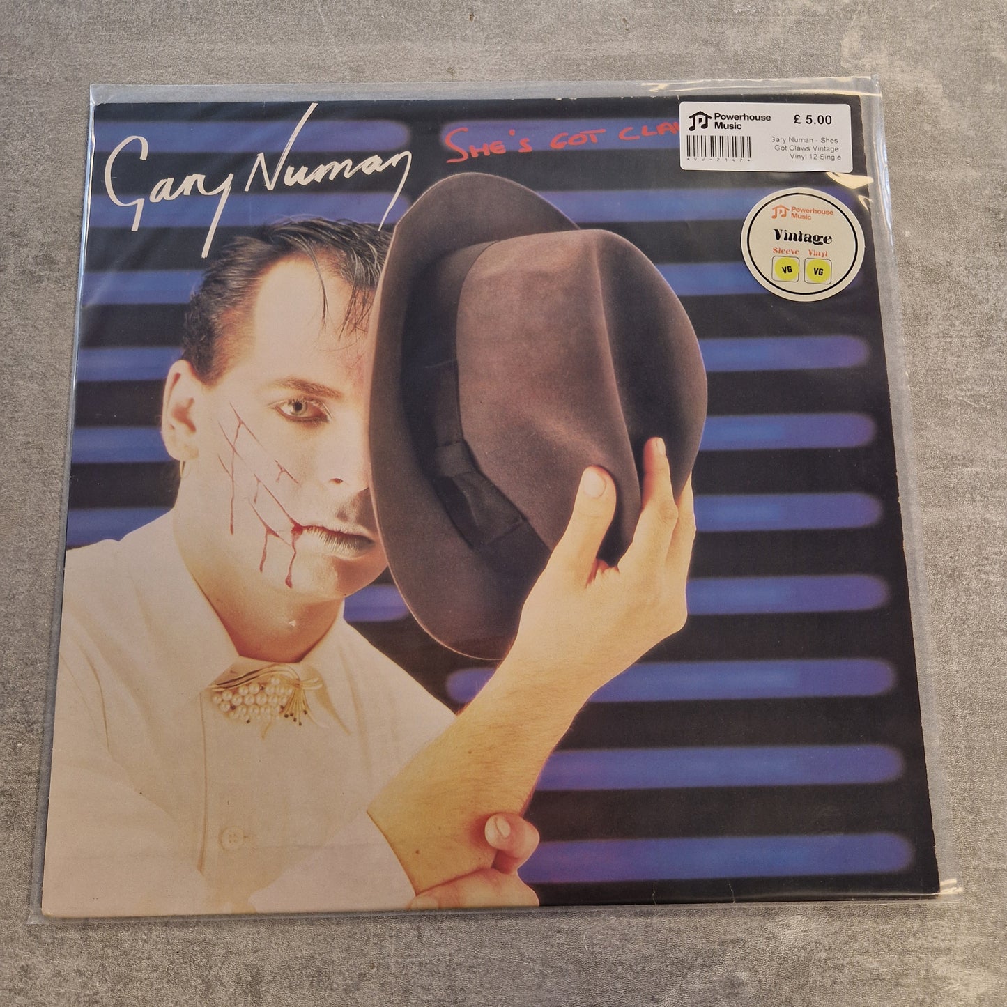 Gary Numan - Shes Got Claws Vintage Vinyl 12" Single A vinyl record sleeve for Gary Numan's 'Smile Again' album, sealed in a clear plastic sleeve, placed on a gray textured surface.
