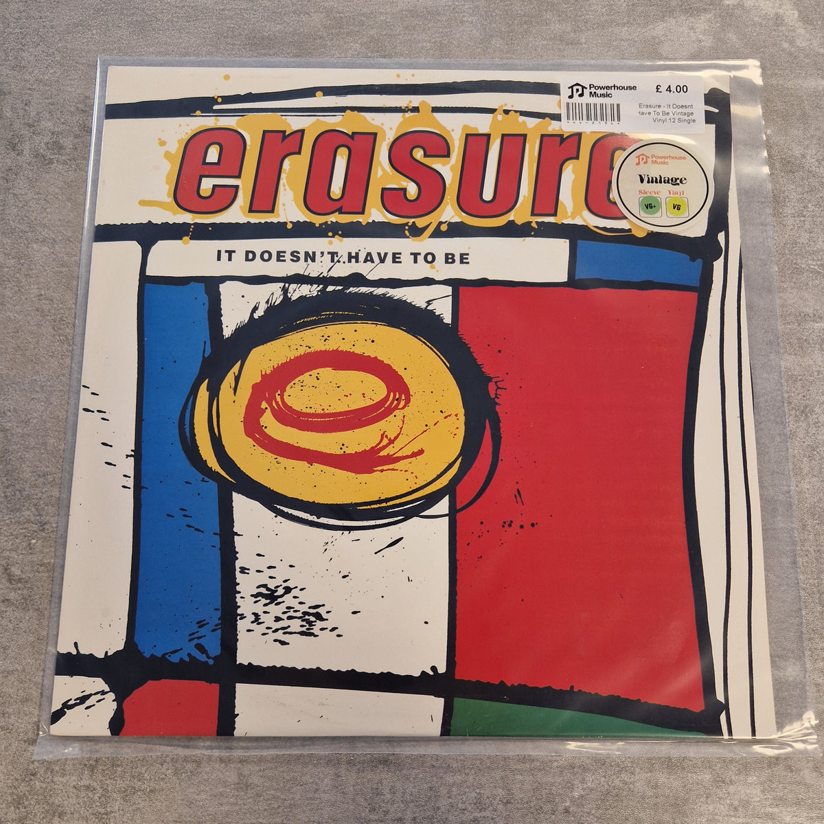 Erasure - It Doesnt Have To Be Vintage Vinyl 12" Single A vinyl record sleeve for Erasure's album 'It Doesn't Have To Be', sealed in a clear plastic sleeve and photographed on a gray textured surface. The cover features a colorful abstract design with red, blue, yellow, and white blocks outlined in black, with the band name 'erasure' in large red letters at the top.