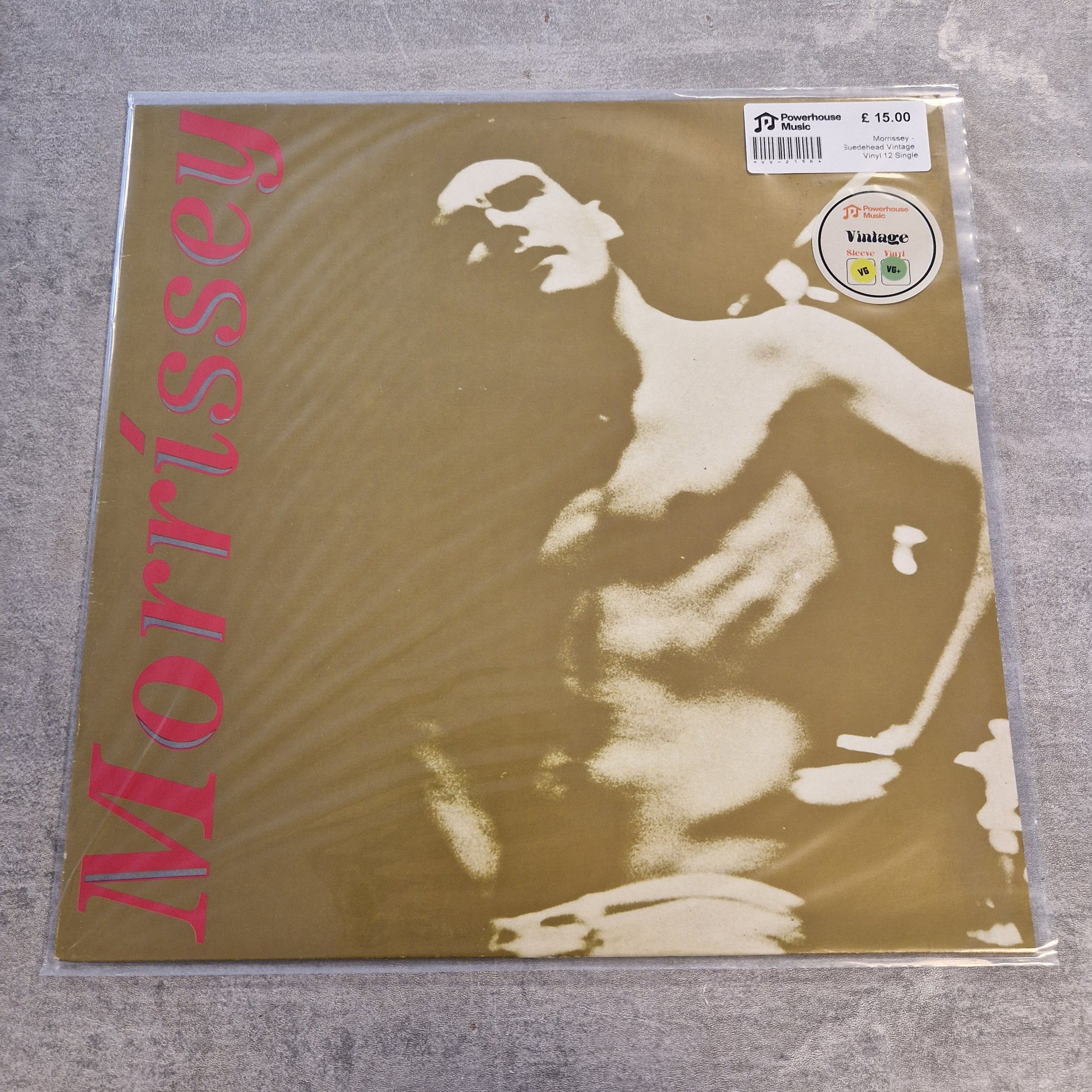 Morrissey - Suedehead Vintage Vinyl 12" Single A Morrissey vinyl record sleeve inside a clear protective plastic sleeve, placed on a gray textured surface. The cover features a sepia-toned abstract portrait of a shirtless figure with the name 'Morrissey' printed vertically in pink on the left side.