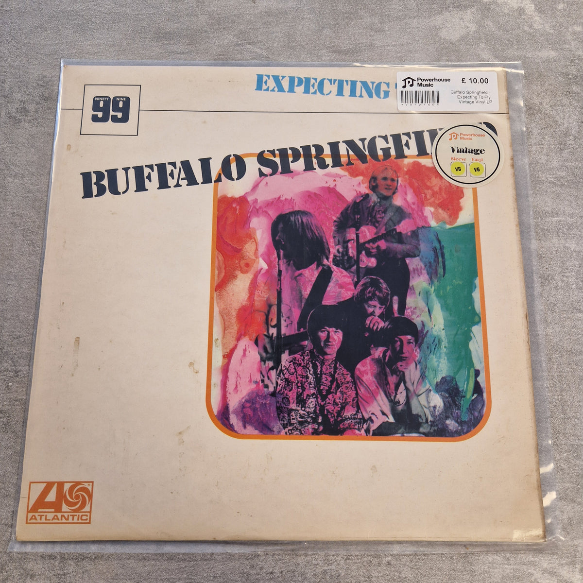 Buffalo Springfield - Expecting To Fly Vintage Vinyl LP A vinyl record sleeve for Buffalo Springfield's 'Expecting' on Atlantic Records, sealed in a clear plastic protective sleeve and photographed on a gray textured surface. The cover is cream-colored with a colorful watercolor-style band portrait in the center and blue/black text.