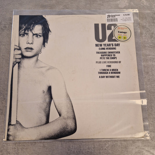 U2 - New Years Day (Long Version) Vintage Vinyl 12" Single A U2 'New Year's Day' vinyl record sleeve in a clear plastic protective case, photographed on a gray textured surface. The cover features a black-and-white portrait of a shirtless young U2 member and track listing text on the right.