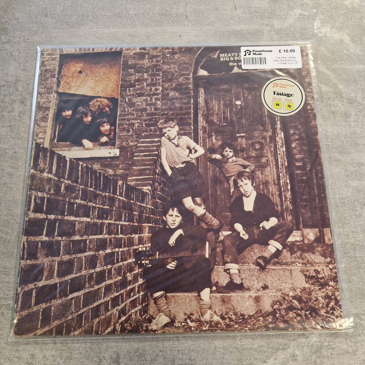 The Who - Meaty Beaty Big & Bouncy Vintage Vinyl LP A vinyl record sleeve for Heavy City Boys' 'Big Boys' on a gray concrete floor. The sleeve features a sepia-toned photograph of four boys posing on a brick wall and wooden door.