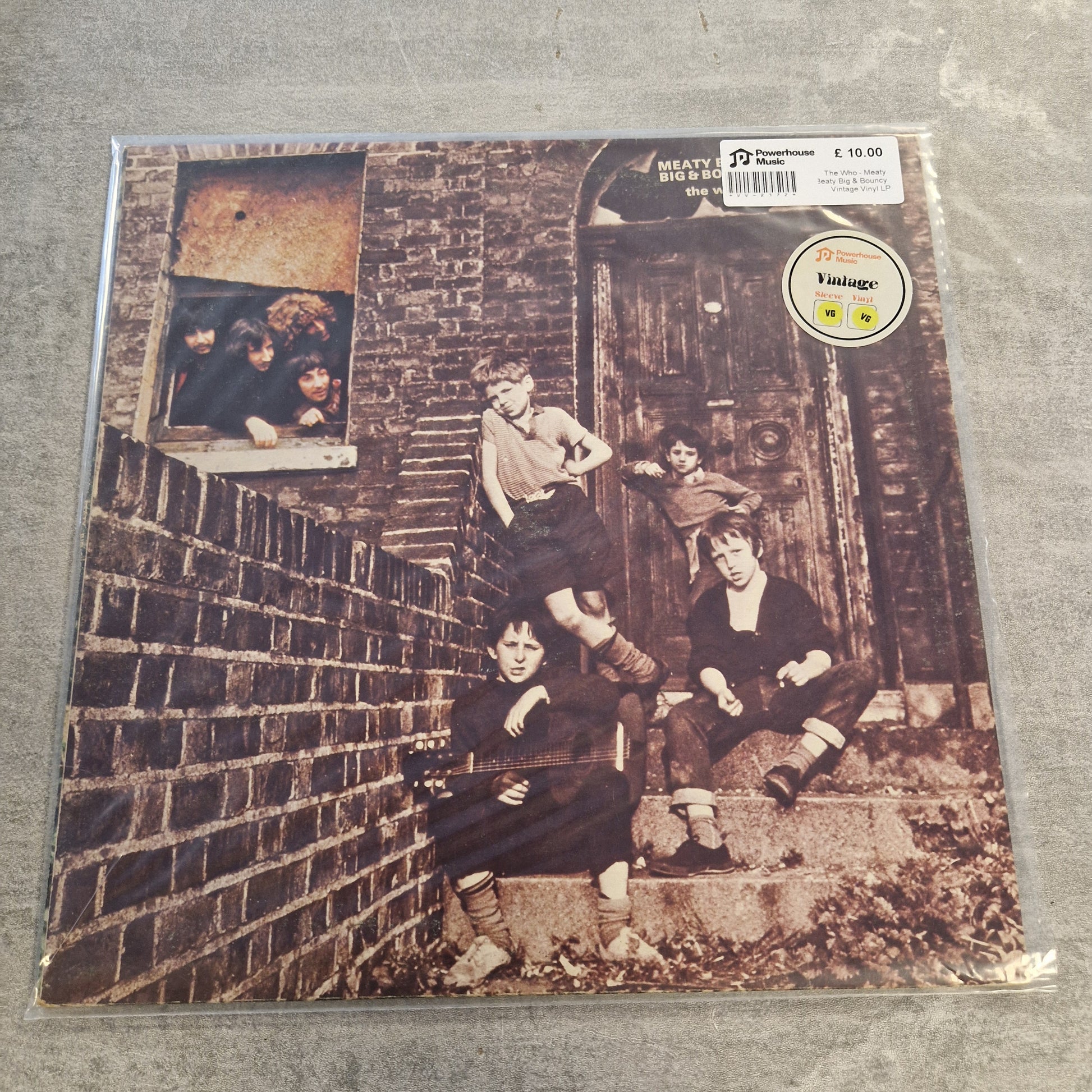 The Who - Meaty Beaty Big & Bouncy Vintage Vinyl LP A vinyl record sleeve for Heavy City Boys' 'Big Boys' on a gray concrete floor. The sleeve features a sepia-toned photograph of four boys posing on a brick wall and wooden door.