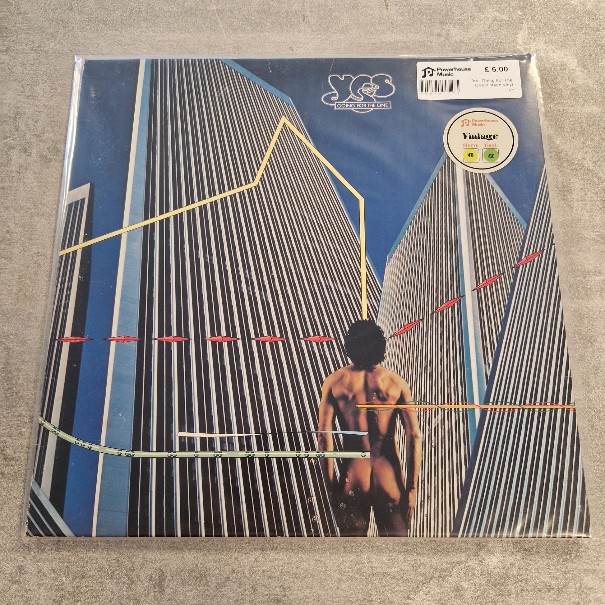 Yes - Going For The One Vintage Vinyl LP A vinyl record sleeve for Yngwie Mosh's 'Kreuz' album, still sealed in its plastic shrink wrap, placed on a gray concrete floor. The cover art features a low-angle perspective of a nude figure walking between two modern skyscrapers under a blue sky, with yellow, red, and green geometric line overlays.