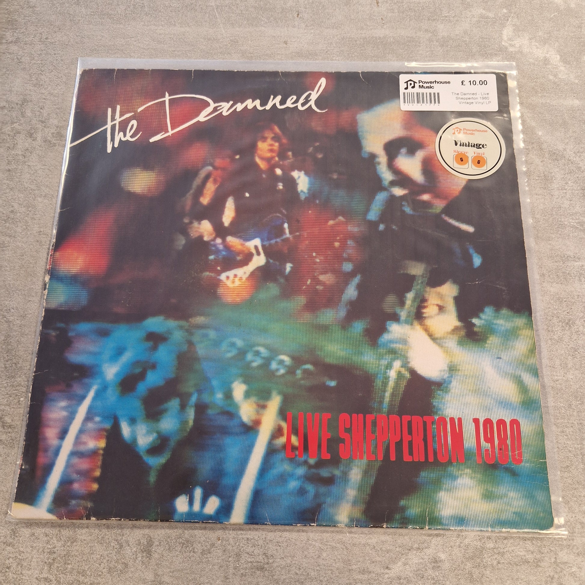 The Damned - Live Shepperton 1980 Vintage Vinyl LP The Damned - Live Snepperton 1980 vinyl record cover, sealed in a clear protective sleeve with a barcode sticker and a Vintage label on the top right, placed on a gray textured surface.