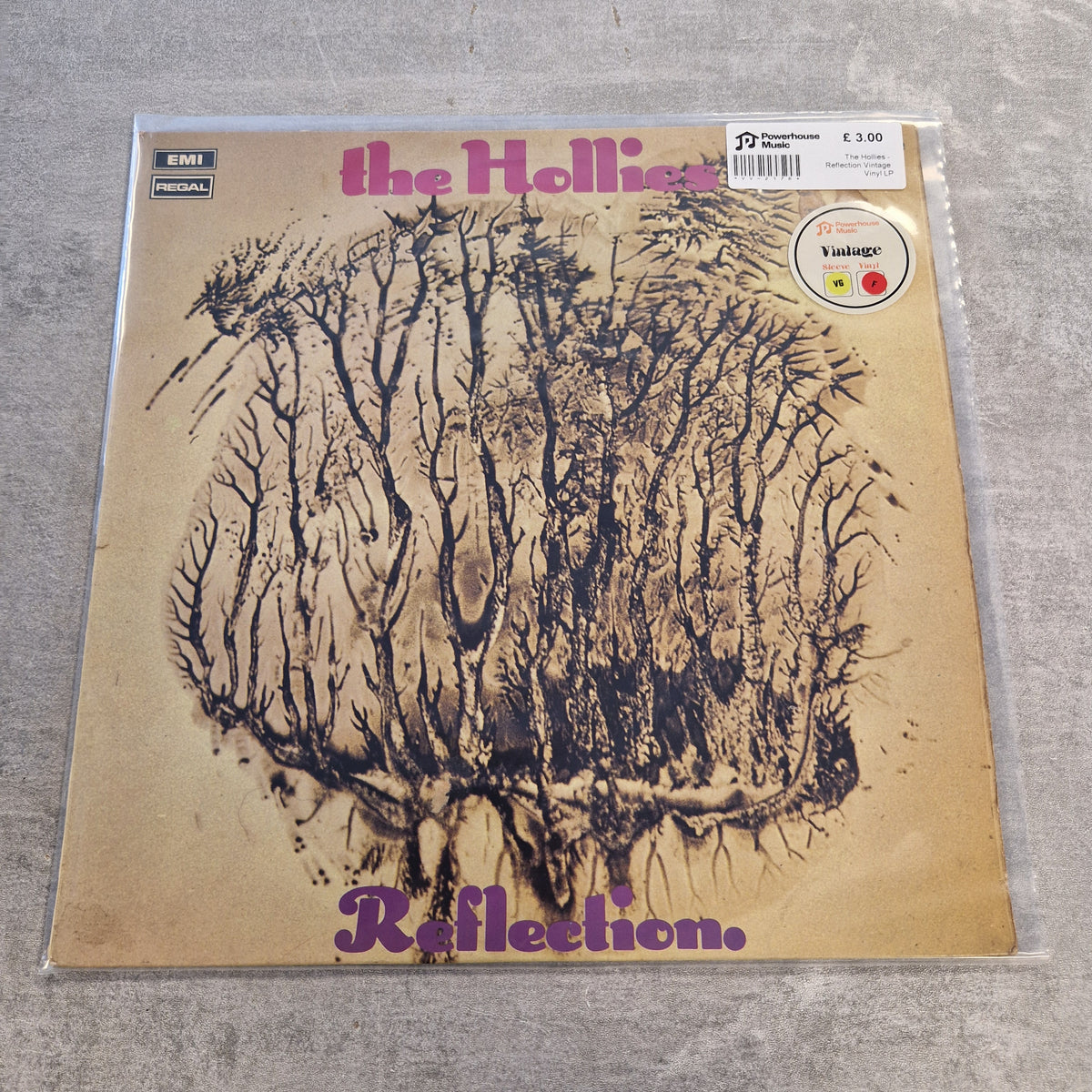 The Hollies - Reflection Vintage Vinyl LP The Holliac 'Reflection' vinyl record album cover, sealed in a clear protective plastic sleeve and photographed on a gray textured surface. The cover features a beige background with a dark brown sketch of a forest and purple text.