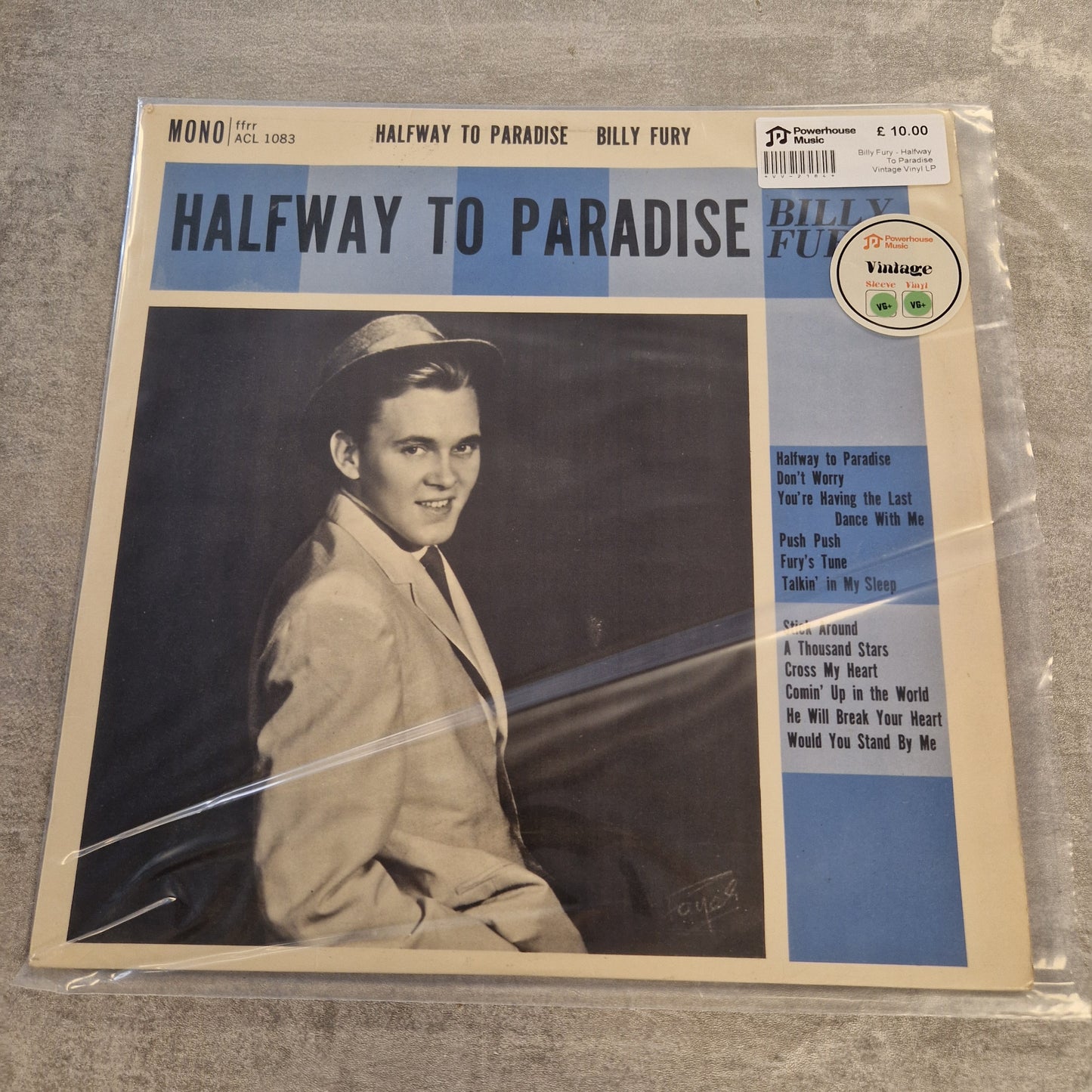 Billy Fury - Halfway To Paradise Vintage Vinyl LP Billy Fury's 'Halfway to Paradise' vinyl record album cover, sealed in a clear plastic sleeve and photographed on a gray textured surface. The cover features a portrait of Billy Fury in a light-colored suit and hat against a dark background, with a blue and beige design and tracklist on the right.