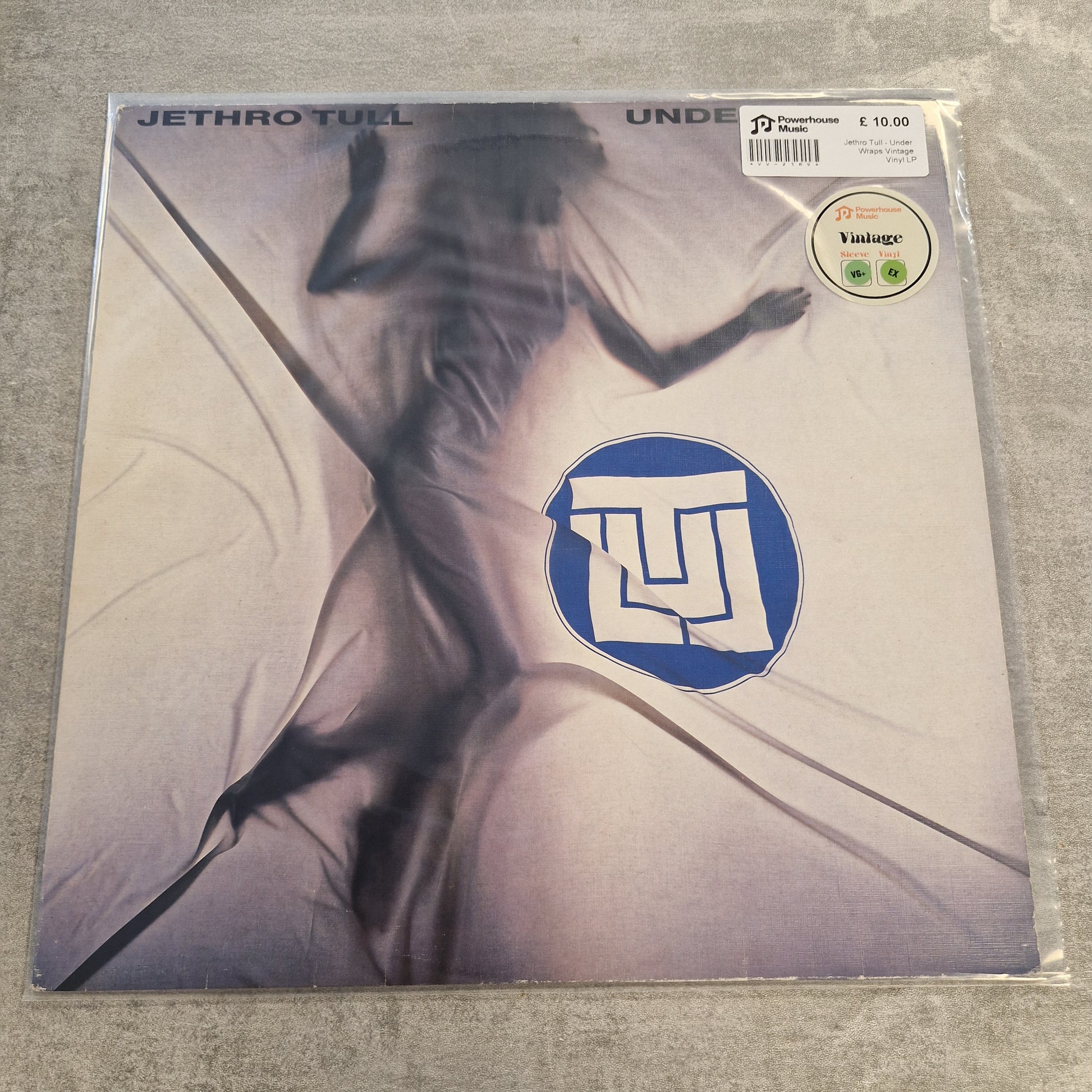 Jethro Tull - Under Wraps Vintage Vinyl LP Jethro Tull - Undenial vinyl record sleeve, showing a stylized figure in flowing white fabric with a blue circular logo. A 7 Records sticker and a Vintage vinyl sticker are visible on the top right, and the sleeve is photographed on a gray textured surface.