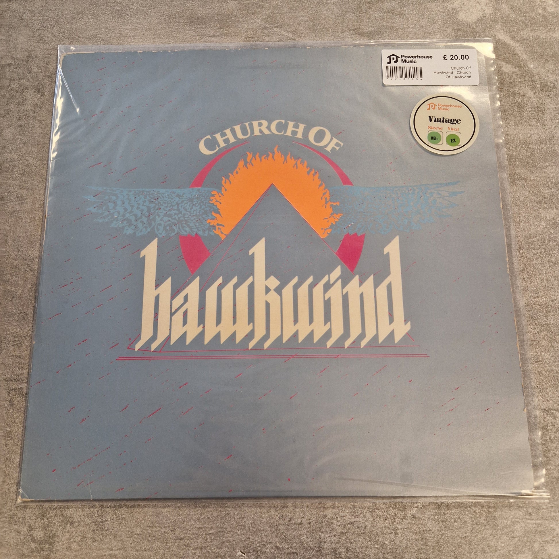 Church Of Hawkwind - Church Of Hawkwind Vintage Vinyl LP A vinyl record sleeve for the band 'Church of Hawkwind' in its original shrink wrap, displayed on a gray textured surface. The cover features a muted blue-gray background with a stylized orange sun, white text, and pink wing details.