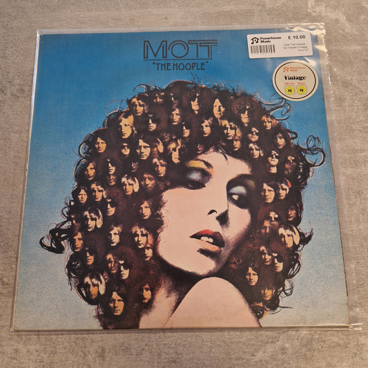 Mott The Hoople - The Hoople Vintage Vinyl LP Mott The Hoople 'The Hoople' vinyl record album cover in its original shrink wrap, displayed on a gray textured surface. The cover art features a striking portrait of a woman with voluminous dark curly hair composed of repeated faces, set against a bright blue background.