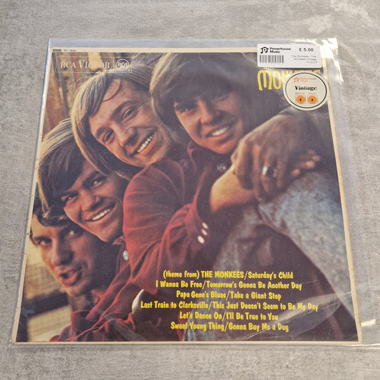 The Monkees - The Monkees Vintage Vinyl LP A vinyl record sleeve for RCA Victor's 'Names from The Monkees / Saturday's Child' album, sealed in plastic packaging and photographed on a gray textured surface. The cover features the four Monkees smiling closely together, with tracklist text in yellow at the bottom right.