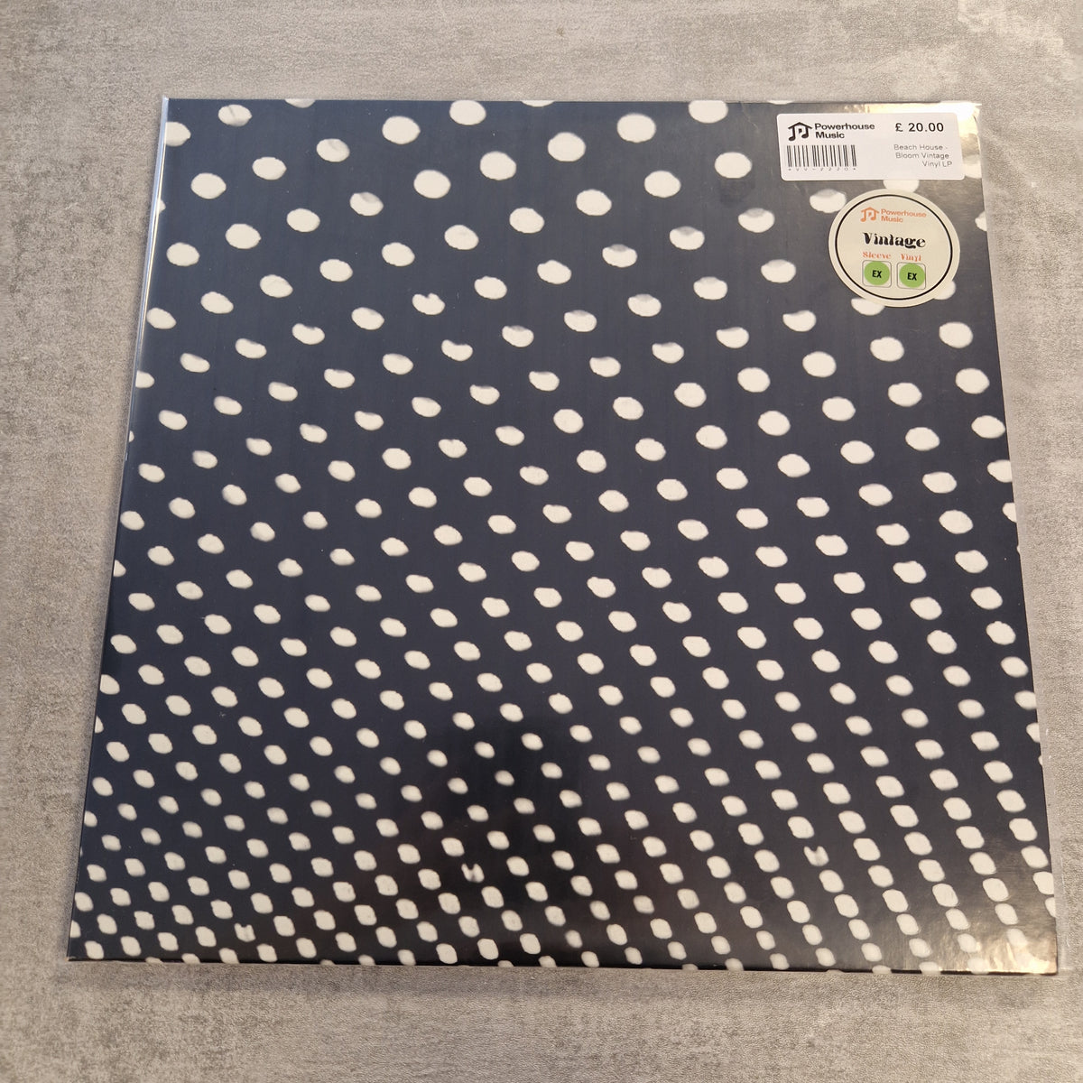 Beach House - Bloom Vintage Vinyl LP A square sheet of patterned paper with a navy blue background and evenly spaced white polka dots, photographed flat on a gray textured surface. A barcode sticker and a round 'Vintage' price sticker are visible in the top right corner.