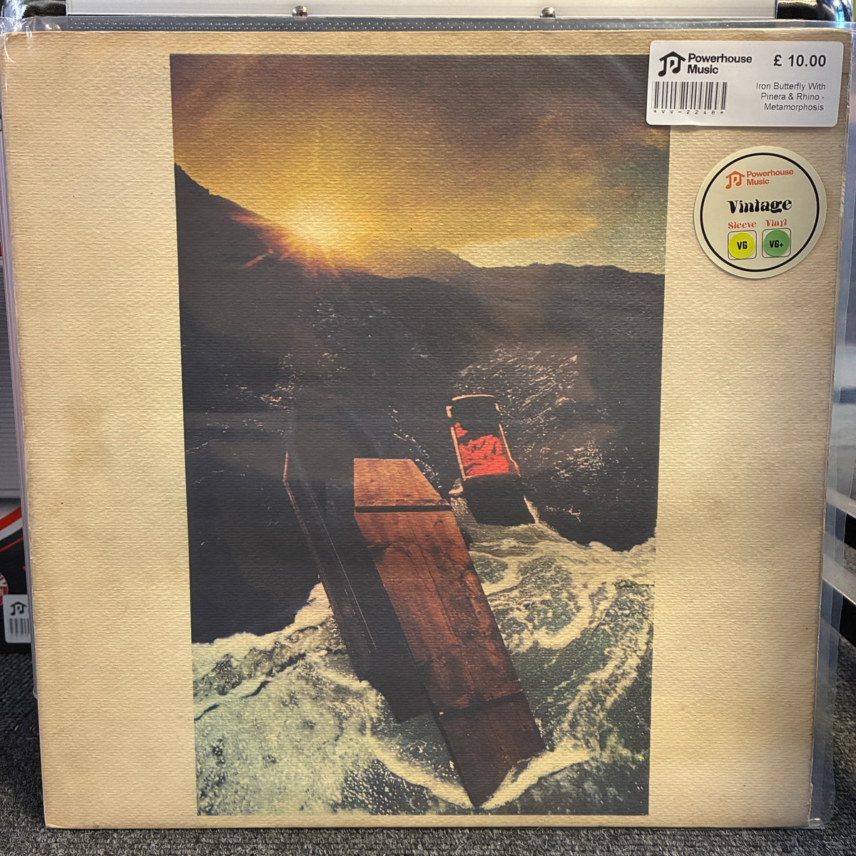 Iron Butterfly With Pinera & Rhino - Metamorphosis Vintage Vinyl LP A vinyl record sleeve for Iron Suede's 'Prinz & Bloch' album, showing a surreal artwork of a car driving over a sinking ship in a stormy sea at sunset. The sleeve has a textured beige border, with a Powerhouse Records sticker and a Vintage sticker visible on the top right.