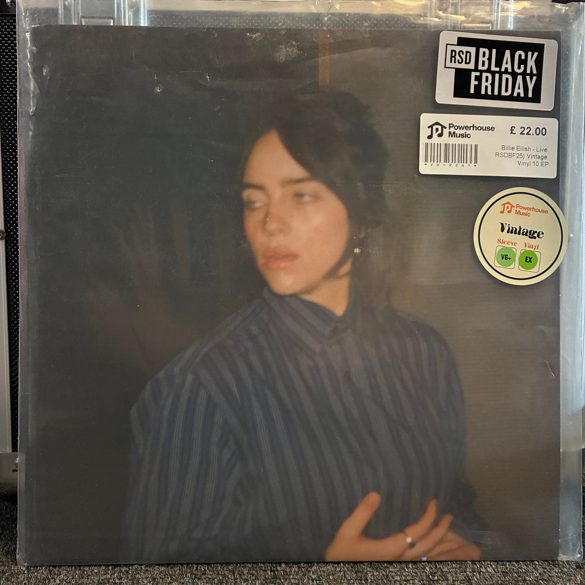 Billie Eilish - Live (RSDBF25) Vintage Vinyl 10" EP A vinyl record sleeve for Billie Eilish's 'Bad Guy' album, sealed in a clear plastic protective sleeve. The sleeve features a dark, moody portrait of Billie Eilish wearing a blue and black striped shirt.