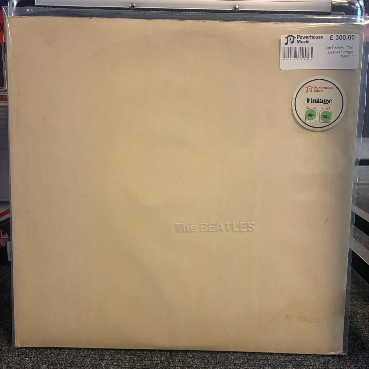 The Beatles - The Beatles Vintage Vinyl LP The Beatles 'The Bedroom Sessions' vinyl record LP cover in its clear plastic shrink-wrap, resting on a dark carpet. The cover is a warm cream/beige color with the band's name embossed in the center.