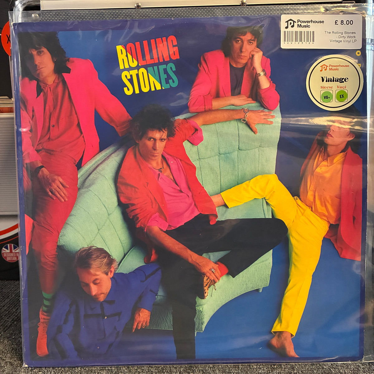 The Rolling Stones - Dirty Work Vintage Vinyl LP A sealed vinyl record sleeve of The Rolling Stones' 'The Rolling Stones - The Times They Don't Believe In Me' on a silver label, photographed on a carpeted floor. The cover art features the band members in bright pink, yellow, and blue outfits against a blue background.