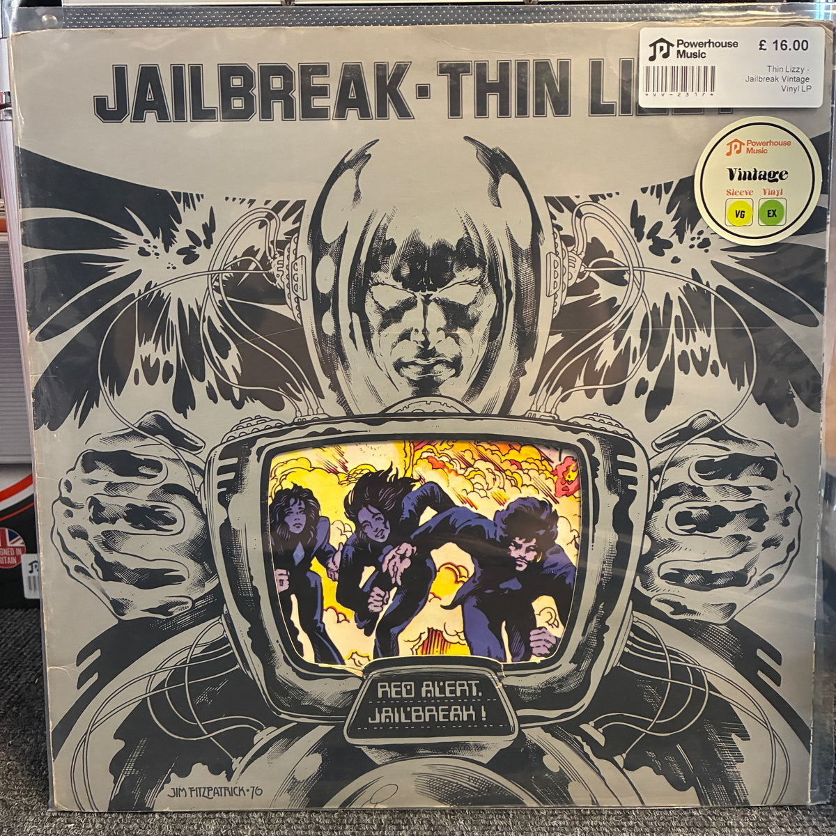 Thin Lizzy - Jailbreak Vintage Vinyl LP Jailbreak - Thin Line vinyl record sleeve photographed on a store shelf. The cover is mostly black, white, and gray with a central illustrated figure and a television screen showing three figures in action.
