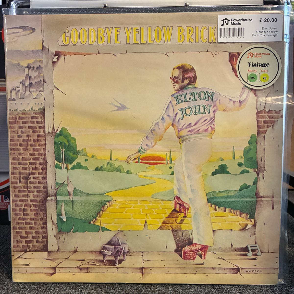 Elton John - Goodbye Yellow Brick Road Vintage Vinyl LP Elton John 'Goodbye Yellow Brick' vinyl record LP cover, sealed in a clear plastic protective case. The cover art features a surreal illustration of Elton John standing in a brick wall looking at a yellow brick road leading through a green landscape.