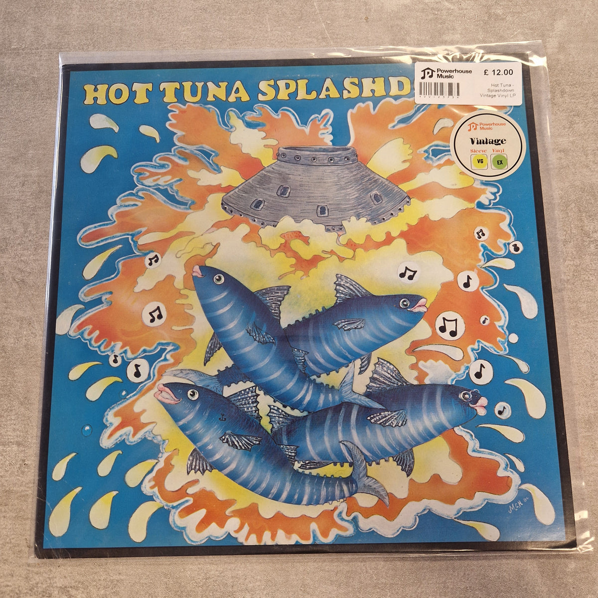Hot Tuna - Splashdown Vintage Vinyl LP A vinyl record sleeve for Hot Tuna Splash's '30 Years Vintage' compilation, sealed in plastic packaging and photographed on a neutral gray surface. The cover art features three blue striped fish swimming through orange and yellow splash patterns with a gray flying saucer above.