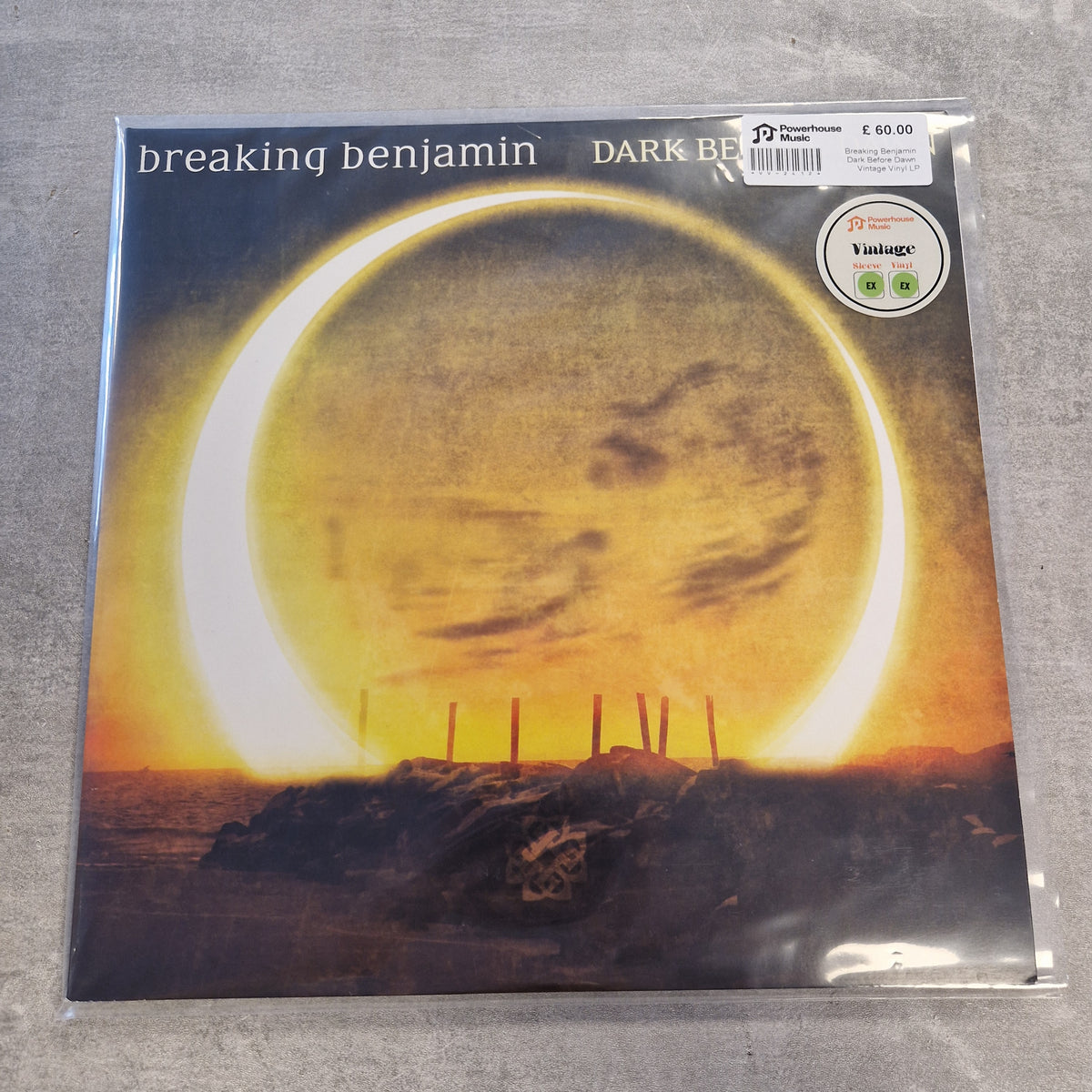 Breaking Benjamin - Dark Before Dawn Vintage Vinyl LP Breaking Benjamin - Dark Beneath the Surface vinyl record sleeve, sealed in plastic with a visible Yachtus sticker and barcode label, placed on a gray textured surface.