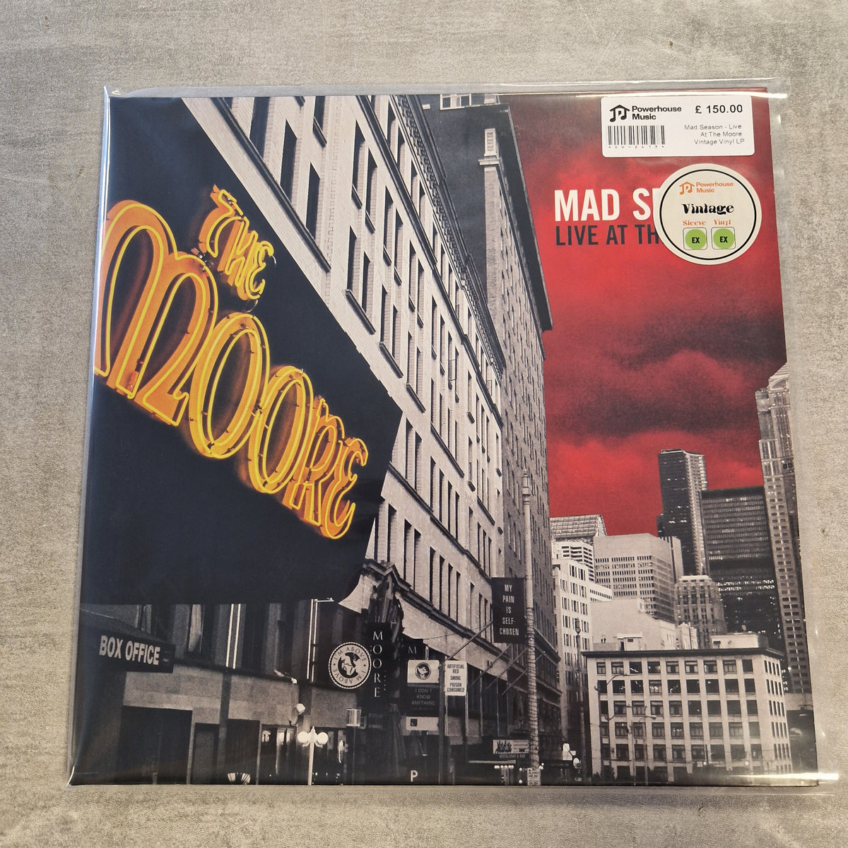 Mad Season - Live At The Moore Vintage Vinyl LP Mad Sweeney's 'Live at the Apollo' vinyl LP cover, sealed in plastic packaging and photographed on a gray textured surface. The cover art features a black-and-white city street scene with a prominent red sky and a large yellow 'The Apollo' sign.