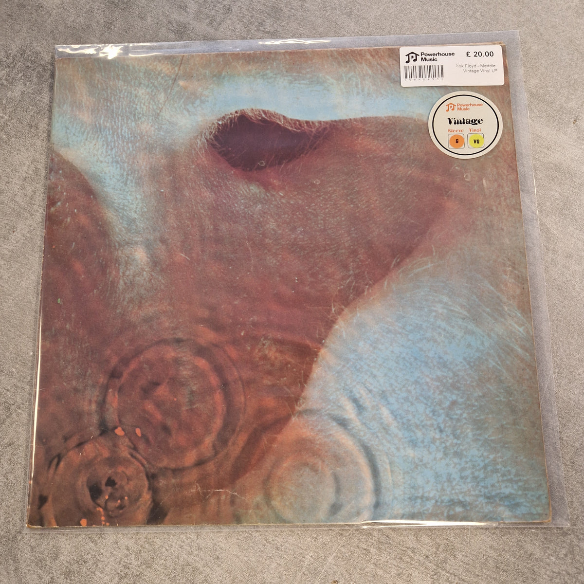 Pink Floyd - Meddle Vintage Vinyl LP A square vinyl record sleeve in clear plastic shrink-wrap, photographed on a gray textured surface. The sleeve features an abstract artwork with a large reddish-brown shape against a light blue background, with a circular sticker label near the top left.